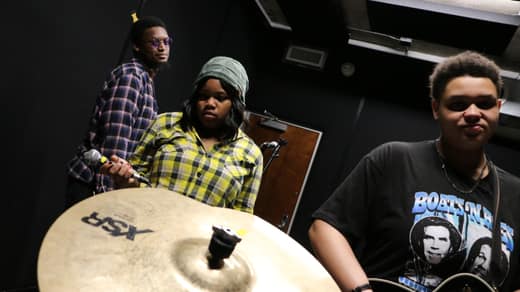Singer holding a microphone between takes, bandmates behind her