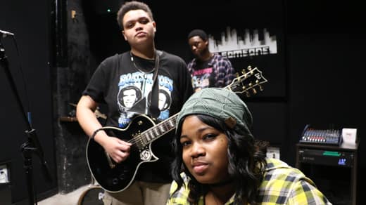 Guitarist with a black Les Paul and singer in a green beanie looking into the camera