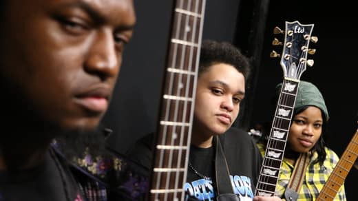 Close-up of three faces between guitar necks, shallow focus