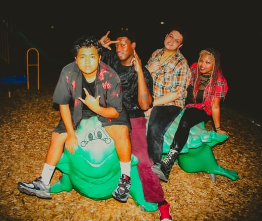 The four band members posed on playground animals at night, lit by flash